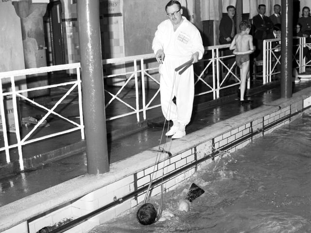 Instructor Norman Sarsfield taching children to swim at Dalry baths using a harness and flippers in January 1966.