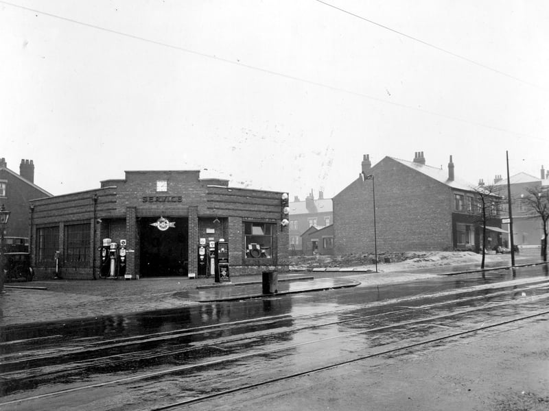 A view across Chapeltown Road from Cowper Street, looking at Savile Service station and garage Art Deco building, petrol pumps, signs, and vehicles can be seen. Pictured in April 1935.