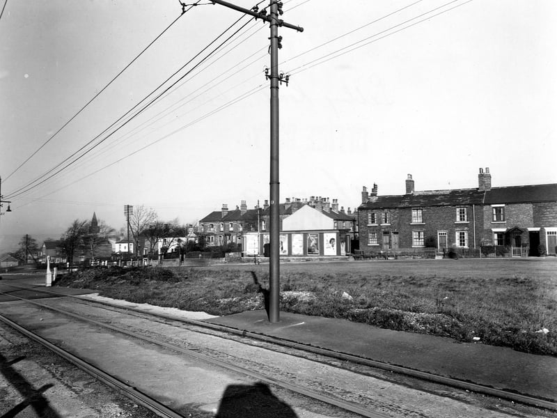 A view looking along Selby Road at the junction with Templenewsam Road from November 1949. A row of advertisements can be seen in the background including army recruitment and Fairy soap. Tram lines and cables are in the foreground on Templenewsam Road.