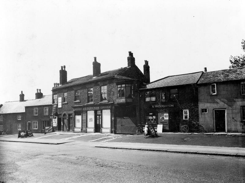 Main Street in June 1936. The premises formerly J.P. Burcham grocer and A. Broughton newsagent. Advertising boards outside shops for cigarettes, including Players and Wills' Woodbines. Two bicycles are outside the newsagents.