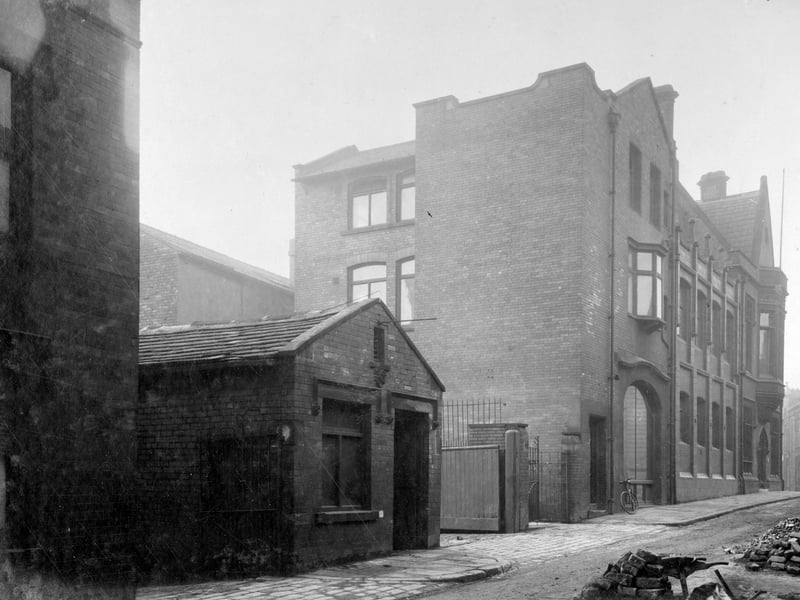 Mark Lane looking up towards Wade Lane in November 1929. This photo shows yards leading off with a mixture of one storey and three storey commercial buildings. There is a bicycle parked against building. Two women stand in distance.