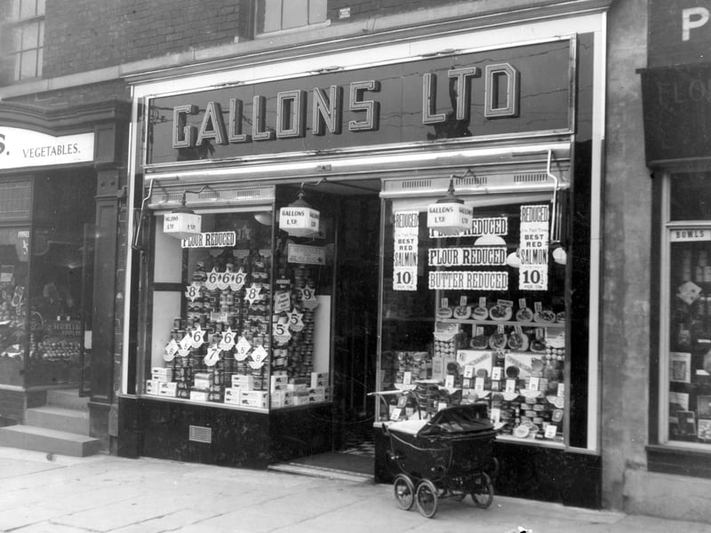 Gallons Ltd, grocers with double fronted glass window displaying wares. On left is Craven Ellis and on right is Smith Thos Wm florist. Pictured in September 1938.