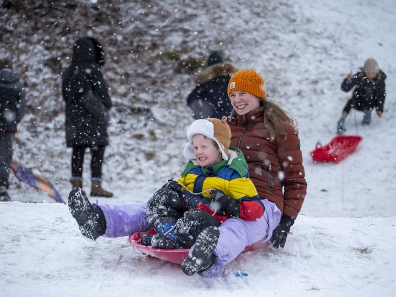 Families enjoy sledging on a grass area in Aviemore town centre