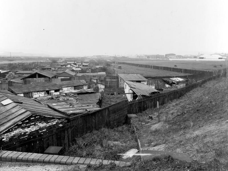 View looking south shows a disused culvert by Mill Green Goit. Various wooden buildings in a state of disrepair are in the foreground. Horses are in a field on the right. Pictured in October 1940.