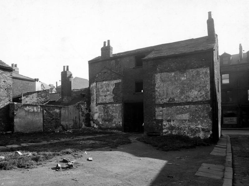 A view of derelict buildings in Holroyd Yard, alongside New Lane. Behind the building can be seen Byford & Hancock, ladies' hairdressers, in Meadow Lane. Pictured in October 1944.