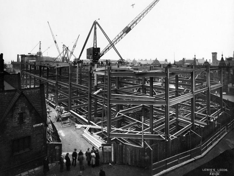 A crowd of onlookers stand at the junction of Wade Lane with Mark Lane, watching the progress being made on the new Lewis's store on The Headrow in November 1931.