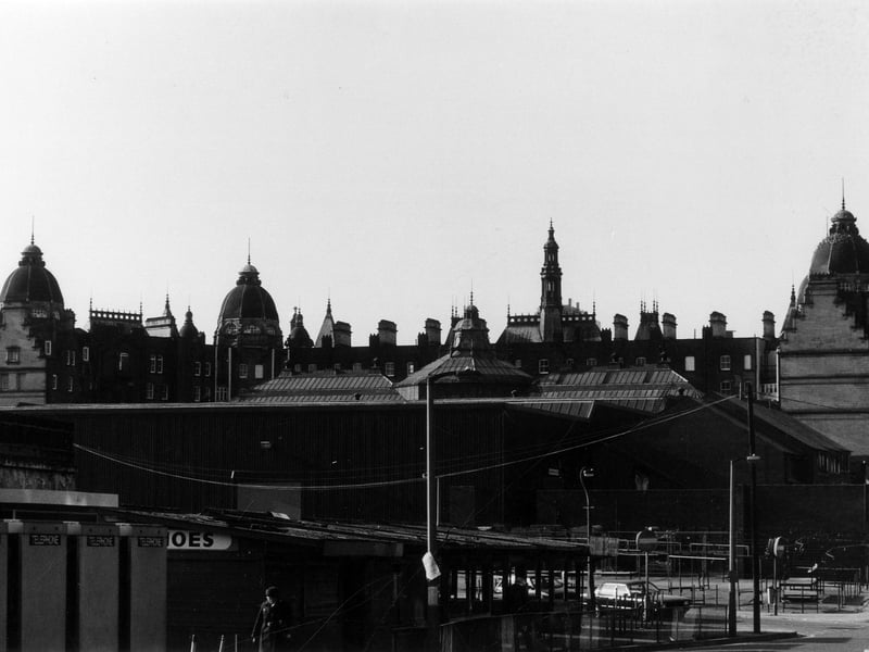 The rear of Kirkgate Market seen from George Street. The outdoor market is visible in the foreground, then Harper Street runs across between this and the indoor market which is seen in the background. Four telephone boxes are lined up on the far left. The shot captures a good view of the rooftops of the indoor market hall, with all domes and chimneys visible.