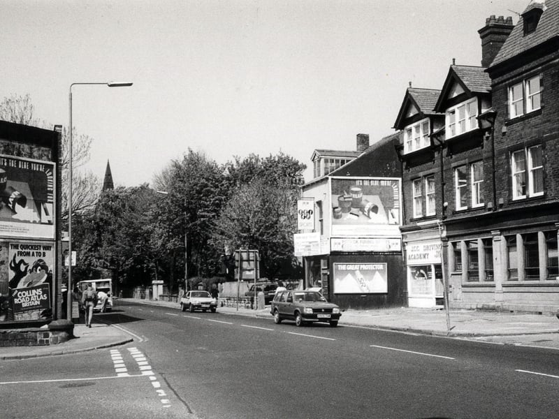 Headingley Lane looking north-west. The junction with Victoria Road is on the left and that with Regent Park Avenue on the right. Advertising hoardings can be seen on both sides of the road while businesses on the right include the J.C.C. Driving Academy.