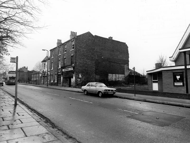 Looking west along Town Street, with the Christadelphian Hall on the right. Further along are the boarded-up premises formerly belonging to G.Bretherick & Son, builders and contractors, then the Barleycorn pub, with houses numbered 116-130 beyond. There is a bus stop on the left, and cars and a bus on the road.