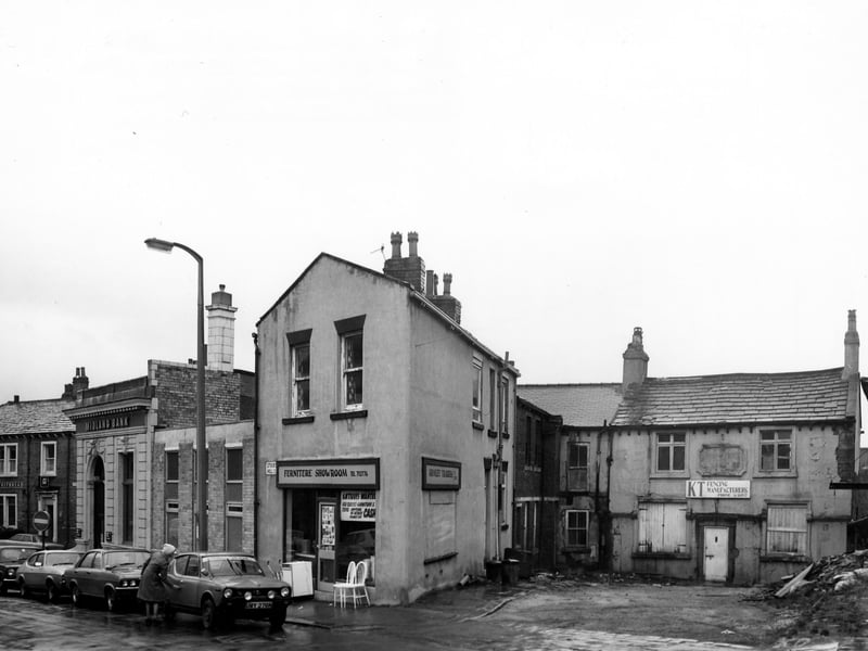 Stocks Hill showing the junction with Crab Lane on the left. On the corner, no. 1 Stocks Hill is the Midland Bank. In the centre is no. 13, Armley Traders second hand furniture, with furniture displayed outside. On the right no. 17 is K.T. Builders and Fencing Manufacturers. The building on the far left is the Malt Shovel public house on Crab Lane.