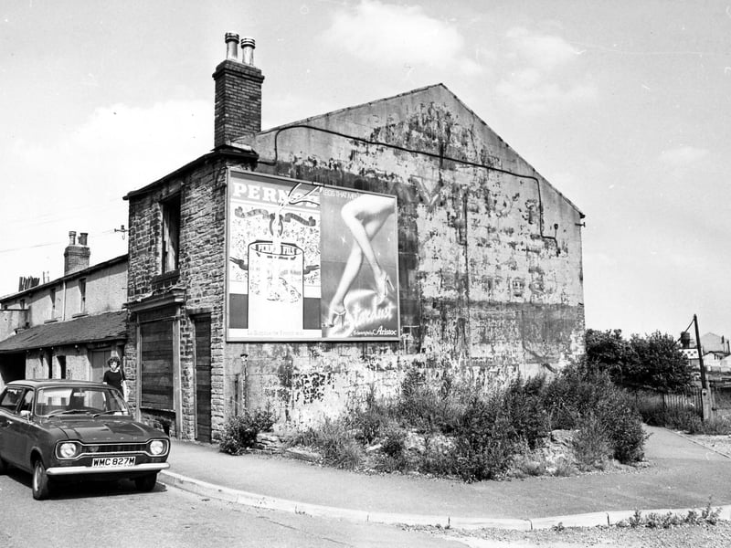 Wortley Road showing No.23-33. No.33 in the foreground is boarded up and has advertisements for Pernod and Aristoc tights on the side. Cars are parked on the road. On the right is Station Road, which formerly led to Armley Moor Station but is now fenced off. Pictured in July 1980.