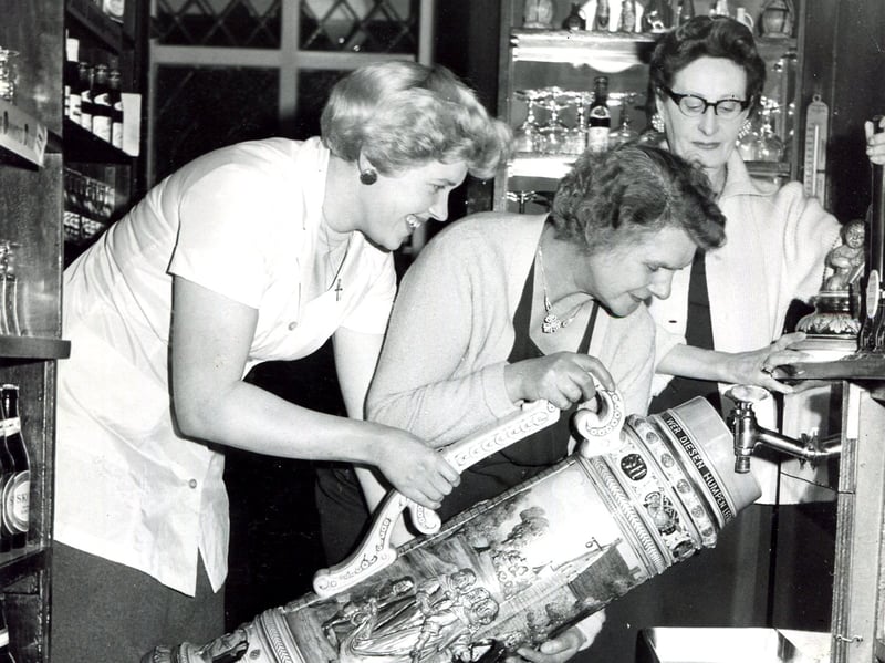 The world's largest beer stein, holding 66 pints, is filled at the Prince of Wales Hotel, Ecclesall Road, Sheffield, in February 1961. Cecil Clift (right), the wife of the licensee, is seen starting  to fill the stein, helped by some of the bar staff.