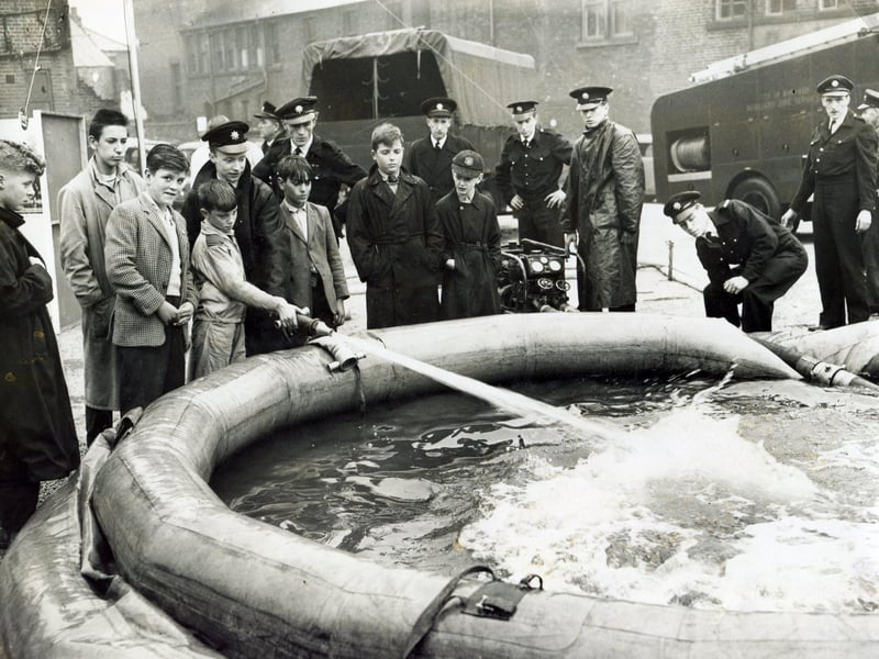 The Sheffield Auxiliary Fire Service give an exhibition on The Moor in October 1961. Youngsters are seen trying their hand at using a hose to fill a portable dam.