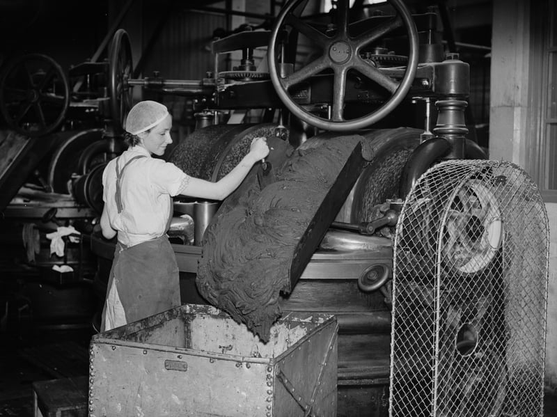 A woman guides a thick stream of melted chocolate down a chute at the Meltis factory, Bedford, in 1936
