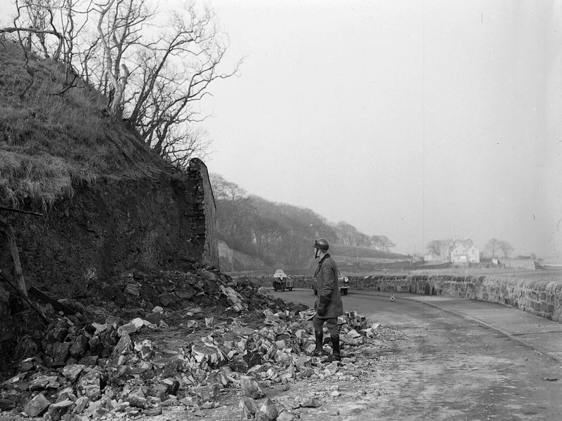 An AA patrolman examines a damaged wall blocking a road in Prestonpans in April 1963.