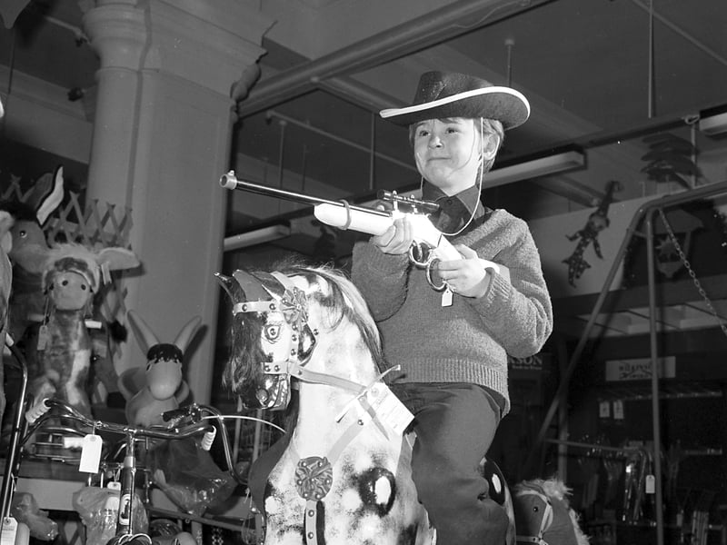 A young boy wearing a cowboy hat and holding a toy rifle on a rocking horse in the toy department of Jenners, Edinburgh, in December 1977