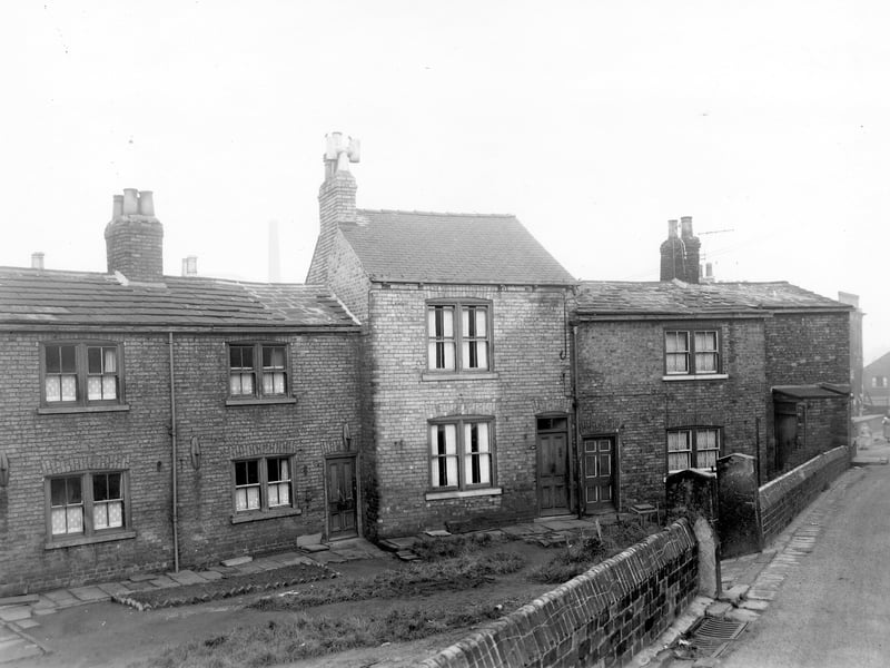 A row of through by light terraced houses on Theaker Lane with a grassed/garden area at the front and a double gateway leading off. Theaker Lane is on the right. Pictured in November 1957.