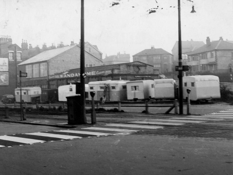 Wandahome caravan sales and supplies at number 121 Stanningley Road. A man stands on a ladder cleaning one of the caravans. A tram stop is to the left of a zebra crossing. Semi detached houses are visible in the background. Pictured in November 1951.