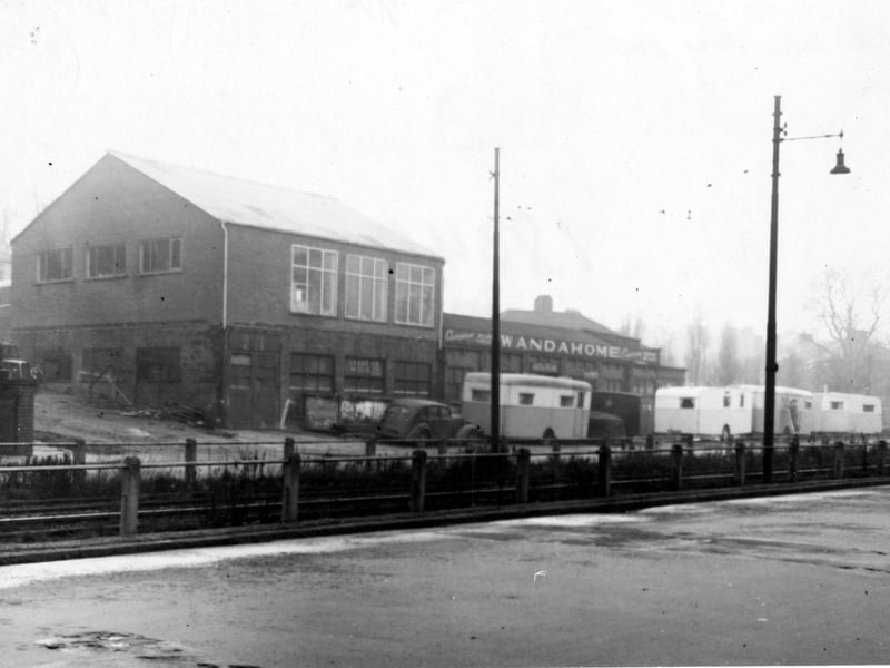 Wandahome caravan sales and supplies at number 121 Stanningley Road. Caravans and a car are visible outside. A central reservation with iron railings divides the road with lamp posts on either side. Pictured in November 1951.