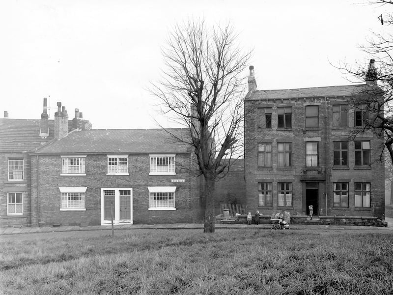 Far Fold in November 1957. On the left of the image are numbers 27 and 28, two through terrace houses with number 29 a large detached run down property on the right. A group of children are gathered in front of number 29 while in the foreground the grassed area of Far Fold Moor is visible.