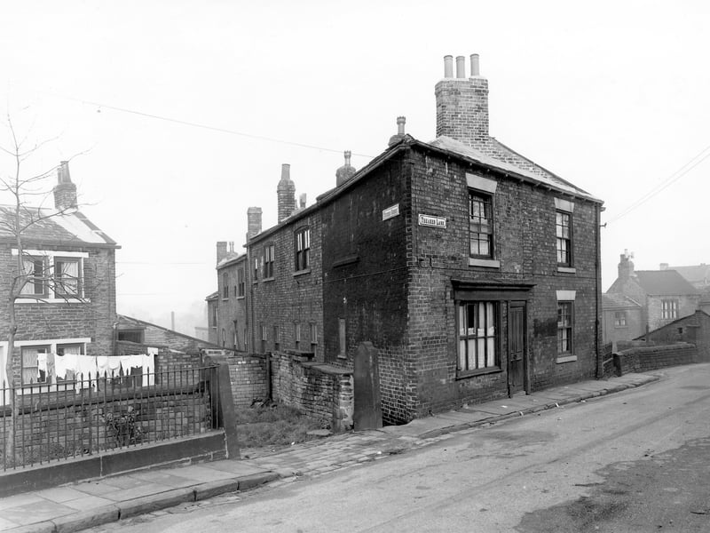 On the left of the image is number 76 Theaker Lane, a through terraced property with a front yard where clothes hang on a line stretched across the space. On the right a gateway gives access to numbers 70, 72 and 74 Theaker Lane at the rear. On the right a ginnel is the start of Winker Green with number 68 Theaker Lane, a triangular gable end building visible on the right. Pictured in November 1957.