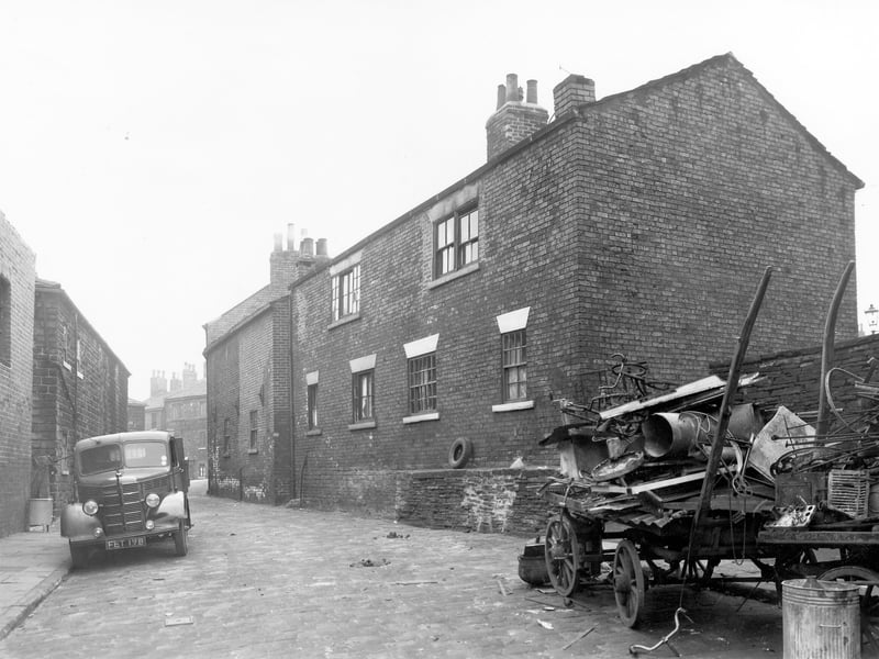 The rear of through by light terraced houses numbers 52 to 58 Theaker Lane. A lorry, reg: FET 178 is parked on the left while on the right stands a cart loaded high with scrap metal. Pictured in November 1957.