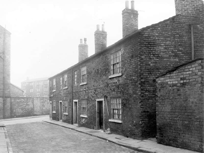 Eyres Place in November 1957. The photo shows a row of four back-to-back terraced houses with the entrance to a shared outside toilet block visible on the right. Visible in the distance is Winker Green Mill on Eyres Mill Side.