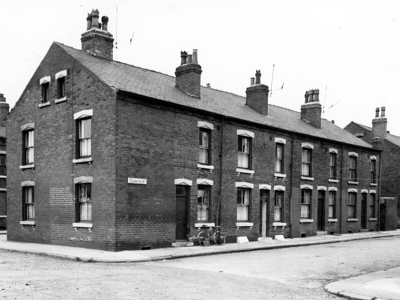 A row of four double fronted back-to-back terraced houses on Falmouth Street with Bridgewater Road on the left and a shared outside toilet block on the right. A bicycle stands under the window of number 9 on the left. Pictured in July 1965.