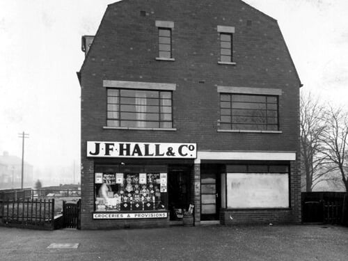 J.F. Hall & Co. grocers at number 24 Foundry Lane, now called Foundry Approach. The shop next door (no. 22) is empty. Harehills Park View is to the left, leading to Coldcotes Avenue and Harehills Park. To the right are the gardens of St. Cyprian's Vicarage. Pictured in November 1937.