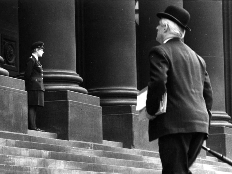 A bowler-hatted gentleman mounts the steps of Leeds Town Hall carrying papers and files, while a uniformed W.P.C. stands on duty at the entrance. The gentleman is thought to be Councillor Patrick ('Paddy') Crotty, a well known local solicitor and Conservative politician.