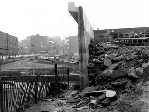 A view of flyover under construction in January 1969 with Bridge Street in foreground and Templar Street to left. In the foreground there are stone, brick, concrete, and wooden pallets. In the middle ground there are pipes and wooden building materials. Business premises on Templar Street are visible.