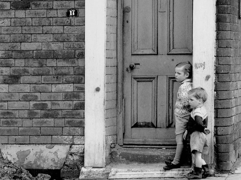 Two small boys stand outside their home at number 17 Rillbank Street, an end red brick terraced house located on the corner with Westfield Crescent.