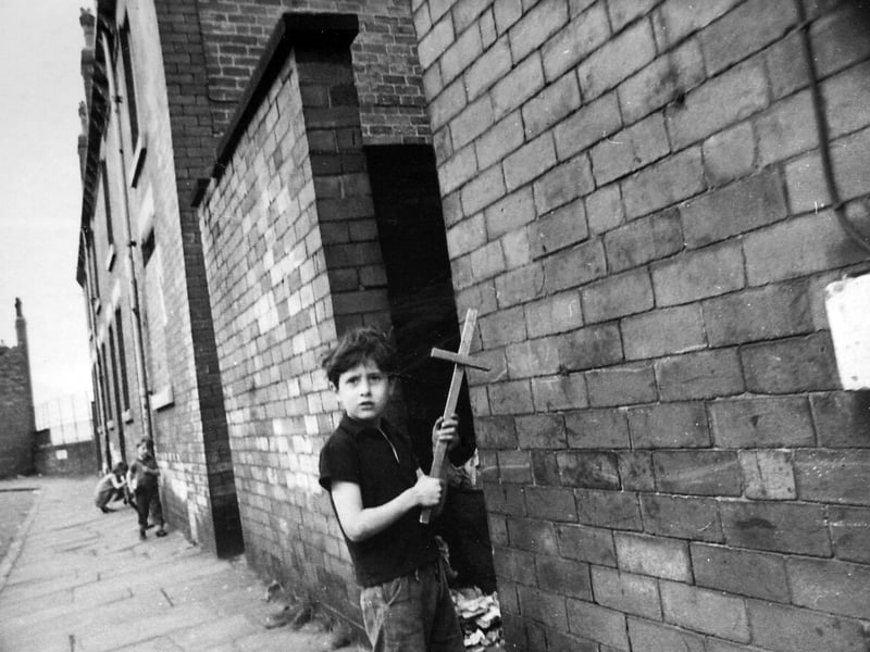 Children playing in the Rosebank Road area. The young boy in the foreground is brandishing a home-made wooden sword. An outside toilet block is seen nearest the camera then terraced houses numbered 88 to 94.