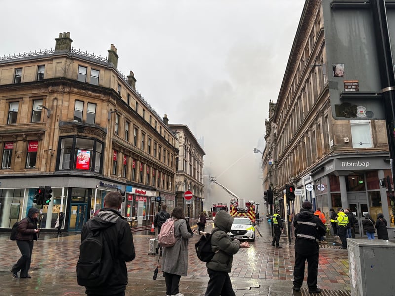 People look at smoke rising as firefighters damp down the remains of a fire which broke out in a building adjacent to Glasgow Central railway station on Sunday. Trains were cancelled following the blaze at a vape shop in Union Street.