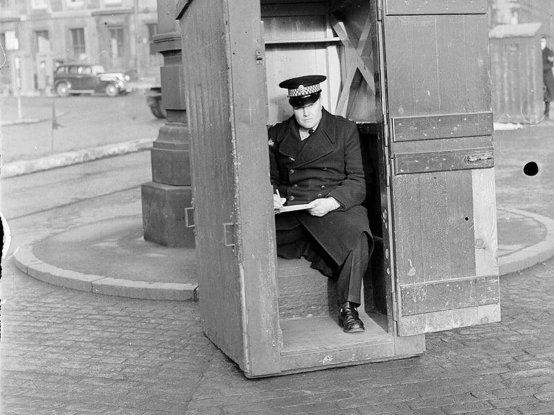 A policeman sitting in a night watchman's hut taking notes on traffic at Haymarket in 1955.