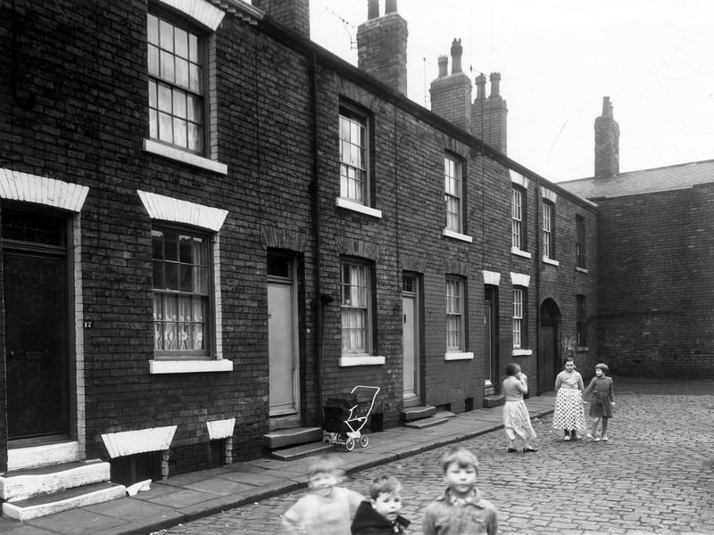 Burley Grove in December 1959. The windows at the right end of the row are at the rear of 26 Lloyd Street. The brick wall at the end is back of houses on Longside Street. Three boys are in the foreground, three girls are also in the street, the one on the right is wearing a pair of adult size high heeled shoes.