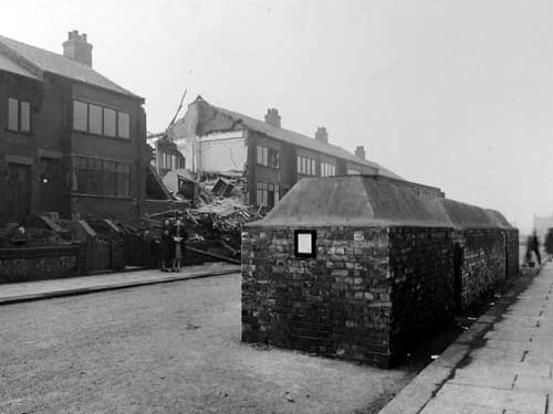 Model Road after the air raids of March 15, 1941, shows remains of nos. 33 - 37. Two women are standing in the foreground, behind air raid shelters built in the road. Joseph Pawson was seriously injured and Harry Thirkettle was killed in the raid. Both were from Model Road.