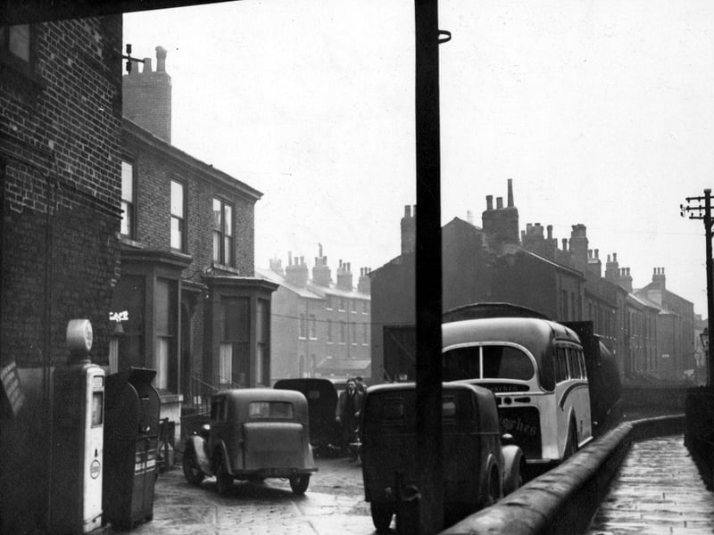 Carlton Garage at Blackman Lane with cars, vans and a small coach in the forecourt. It also has a petrol pump. In the background are terraced houses. To the right, down the narrow passageway, are houses on Carlton Grove, these were later demolished for the building of the Inner Ring Road. Pictured in December 1953.