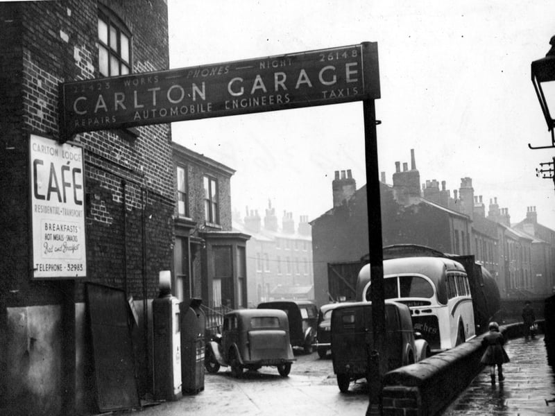 Carlton Garage, automobile engineer of Blackman Lane with sign for repairs and taxis. On the forecourt are cars, vans and a small coach and petrol pumps. Next door is the Carlton Lodge cafe, offering bed and breakfast and meals. Pictured in December 1953.