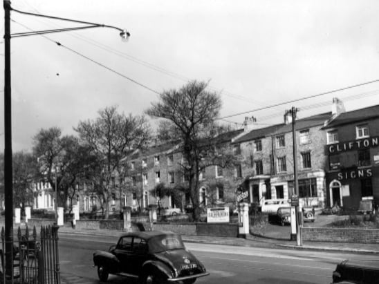 Looking north at numbers 4 to 18 Blenheim Terrace, off Woodhouse Lane in November 1955. Properties visible are number 4, Clifton Signs, number 5, British Legion, West Riding County Office. A Morris Minor convertible car is parked in the foreground. Others are parked in Clifton Signs car park.