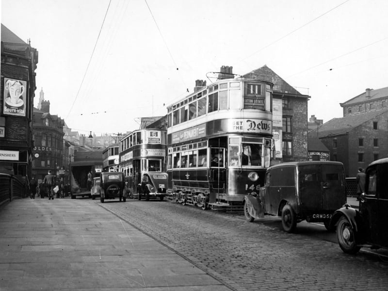 Looking north from Leeds Bridge onto Briggate in November 1949. Trams, cars and vans are visible. The trams include the number 11 to Gipton Estate and number 6 to Meanwood. Advertisements are on the trams for The News, Leeds Permanent, Melbourne ales and one for the beverage, Bournvita, is visible on the left.