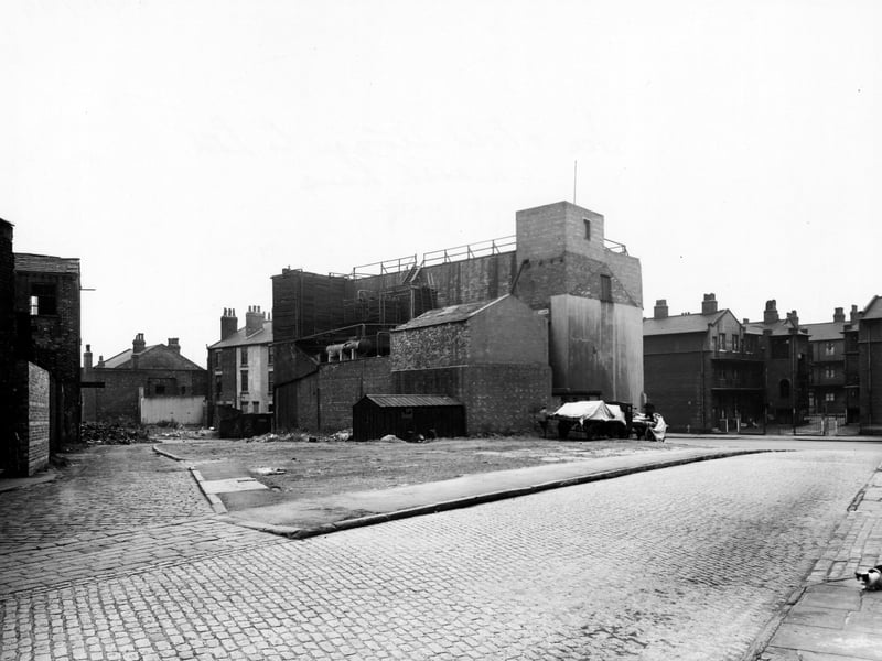 Looking North-West along Mill Street in October 1949 , with Cawood Street Yard to the left. Two lorries are parked in the distance with white sheets covering their load. A cat can be seen in the bottom right hand corner.
