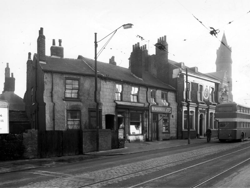Dewsbury Road in December 1958. On the left is a back-to-back private residence. At number 133 is R. Bottom, fish salesman where a man in a flat cap and apron stand in the doorway. On the right at number 135 is W. Murrel, gents hairdressing saloon, note the striped pole. On the corner at number 137 is the Junction Hotel, a melbourne ales inn. A bus pulls up to the junction with Moor Road and in the distance can be seen the spire of St Peters Church.