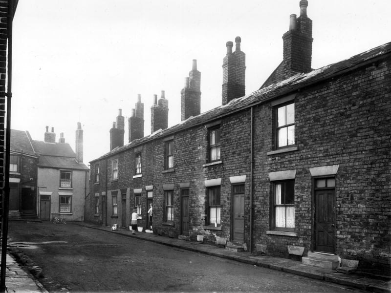Drayton Manor Yard in December 1958. A childs tricycle stands outside number 13. While another smaller one sits outside number 2. Two women stand chatting in the doorway of number 3.