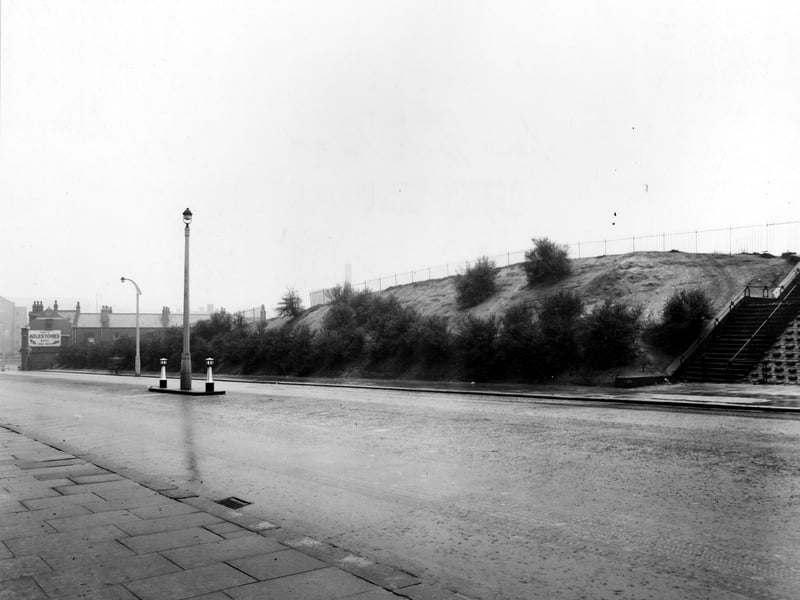 This photo from November 1949 looks north west along New York Road from Quarry Hill flats with close up of pavement. Central bollards and paving in middle of road and sloping bank with shrubs and steps up other side.