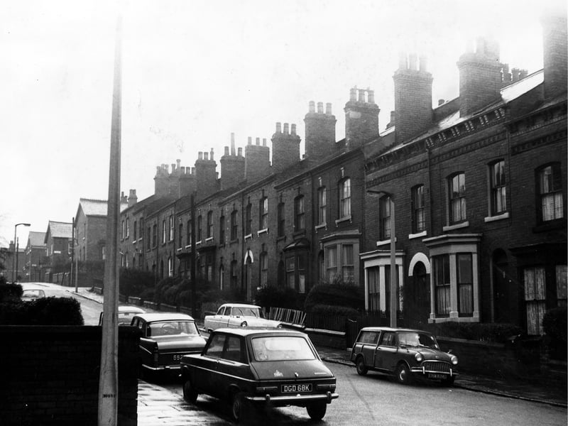 A row of through terraced houses on Edwin Road some with bay front windows. Each house has a private front yard and a variety of cars parked on the street.