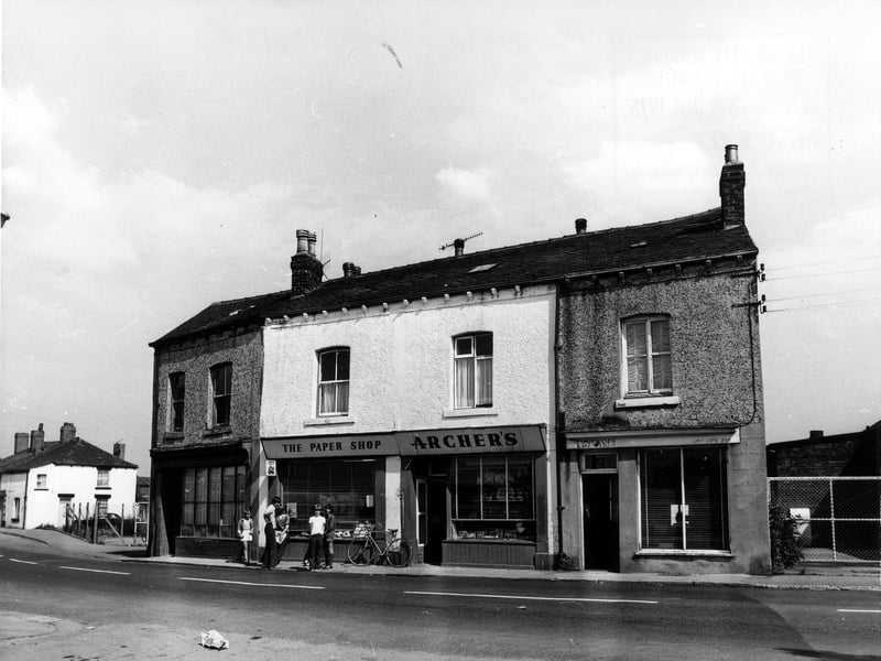 Main Street pictured in July 1975. Shops include Archer's 'the paper shop' at nos. 12-14 in the centre, outside which a group of children are standing.
