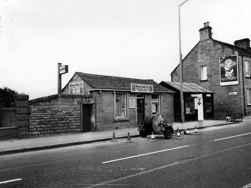 The north-east side of King Street in August 1981. In the centre is a single-storey stone building housing the Halifax Building Society and Newsome Clough & Son, insurance brokers and estate agents. Moving right, another single-storey building is occupied by Eileen's haberdashery. On the far right, is Drighlington Post Office.