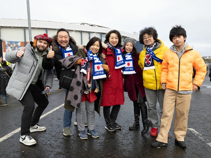 A Scotland fan gatecrashes a photo of the Japanese away support.