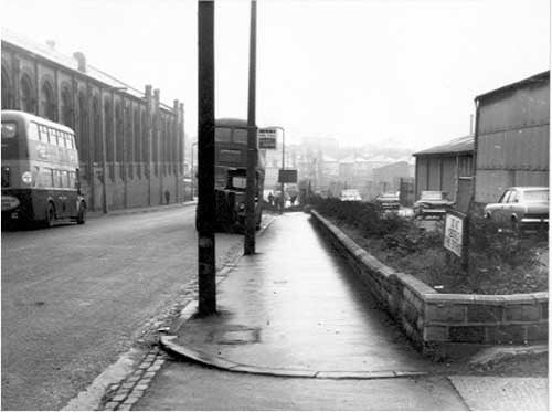 Looking south east along Henconner Lane between Bramley bus station and Forest Products timber depot. Double decker buses on either side of the road. Bus stop and "do not obstruct this entrance" sign visible. Pictured in November 1968.